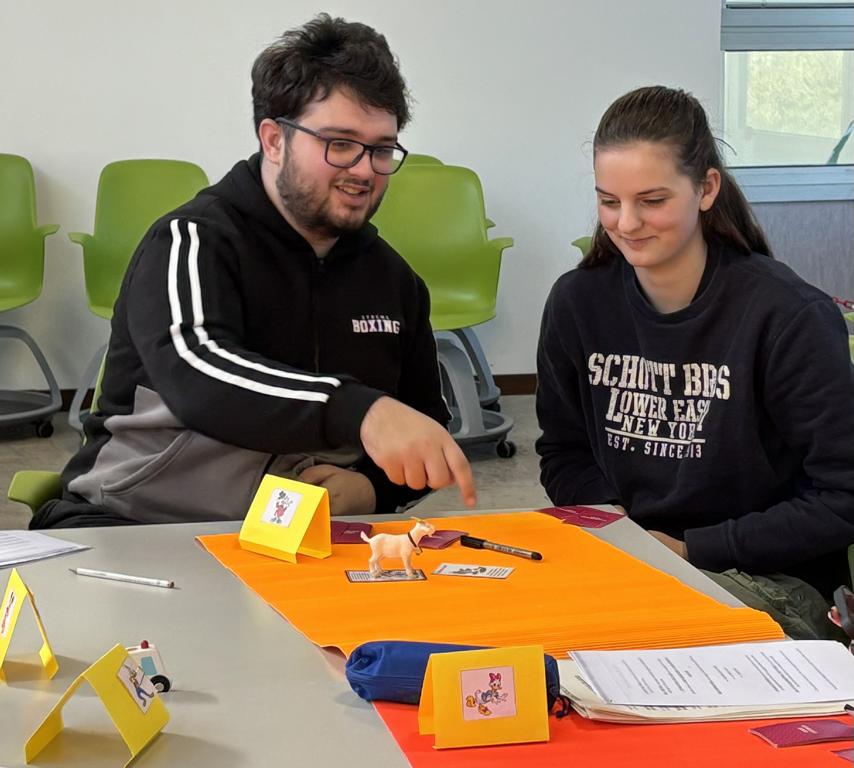 Zwei Teilnehmende sitzen an einem Tisch und bearbeiten gemeinsam eine interaktive Lernaufgabe mit Karten und Materialien. Dabei tauschen sie sich aus und entwickeln Lösungen.