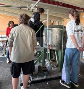 Mehrere Teilnehmende stehen an einer Maschine zur Papierherstellung und beobachten den Prozess.