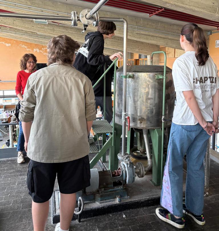 Mehrere Teilnehmende stehen an einer Maschine zur Papierherstellung und beobachten den Prozess.