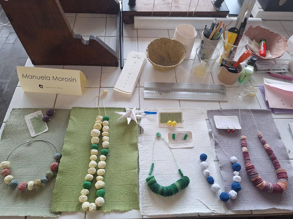 Verschiedene Schmuckstücke und Gegenstände aus Papier liegen auf einem Tisch ausgestellt.