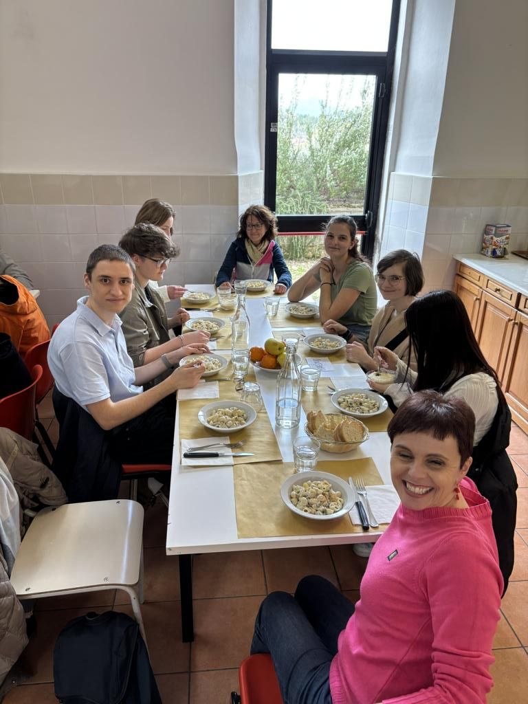 Eine Gruppe von Teilnehmenden sitzt gemeinsam an einem Tisch in der Schulmensa und isst ein warmes Mittagessen.