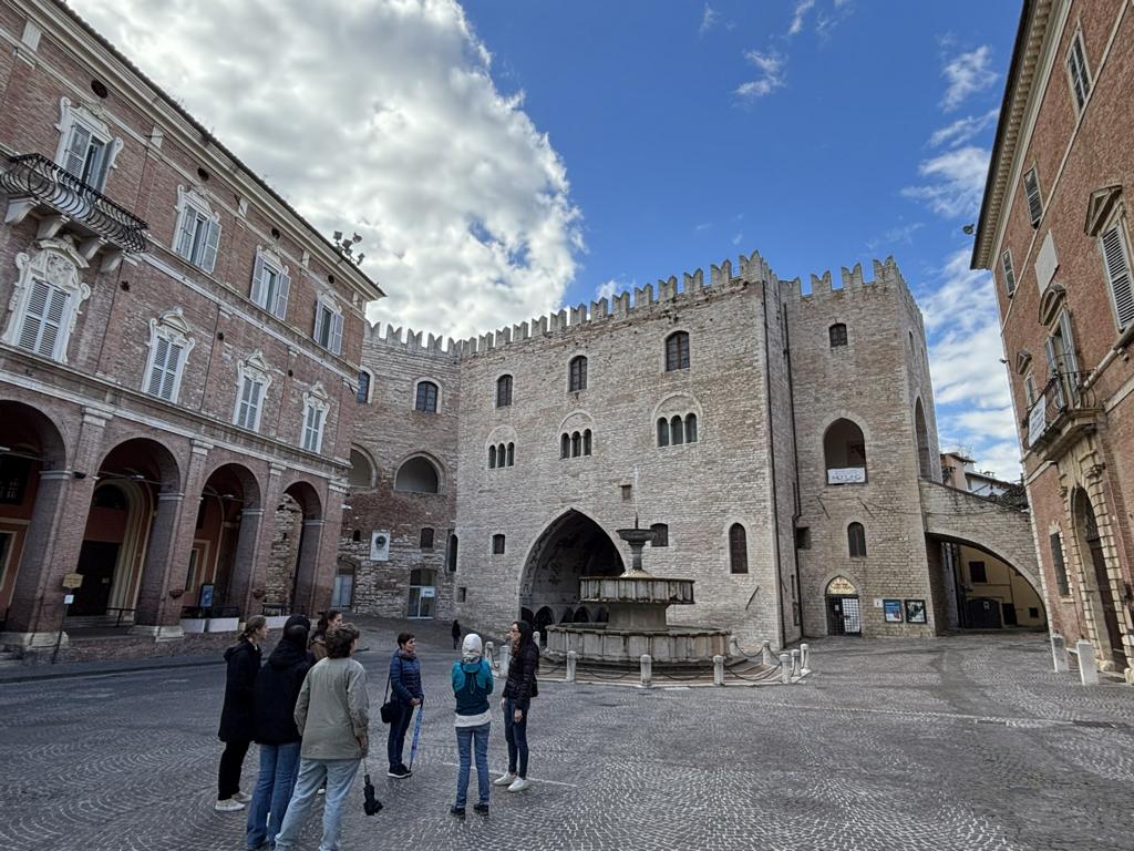Teilnehmende des ERASMUS-Austauschs erkunden einen historischen Platz in Fabriano mit mittelalterlicher Architektur und einem Brunnen im Zentrum.