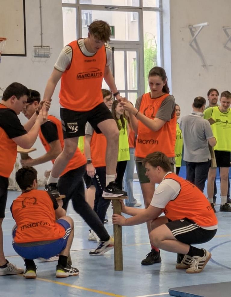 Mehrere Teilnehmende unterstützen sich gegenseitig bei einer sportlichen Übung in einer Turnhalle.